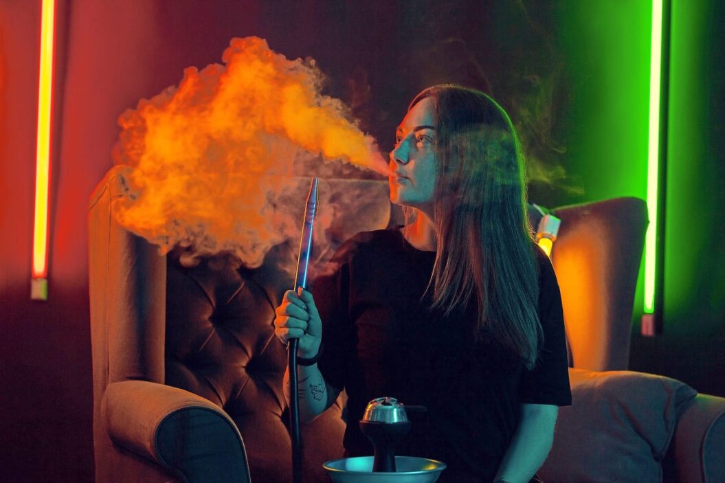 Pretty girl in a black t-shirt is smoking a hookah exhaling a smoke at a luxury night club